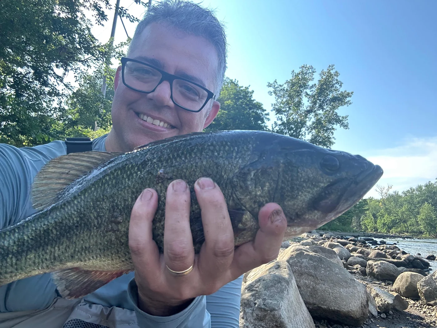 Ackley Will smiling while holding a fish beside the water